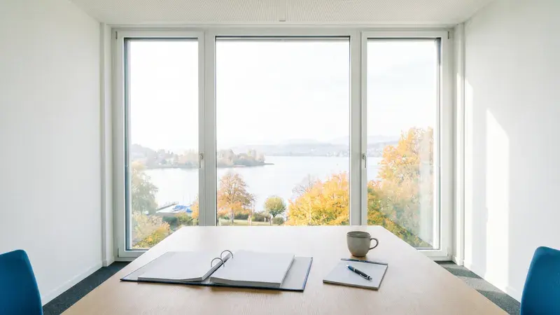 Heller Besprechungsraum mit Blick über den Zürichsee, auf dem Tisch ein offener Ordner und ein Notizblock